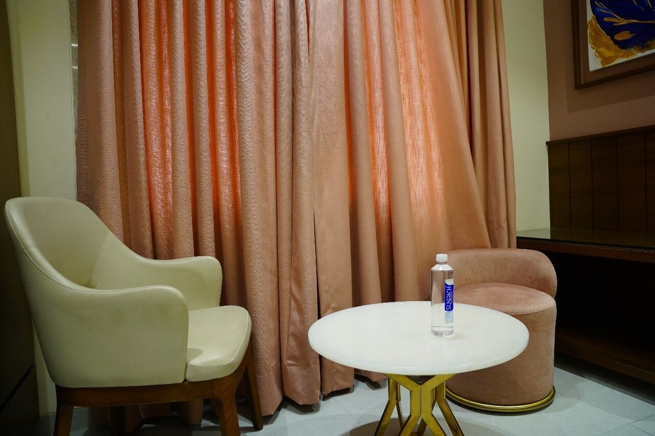 Una habitación con una mesa blanca redonda, dos sillas, una botella de agua y una cortina.