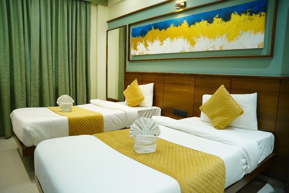 A hotel room with two beds, each with white linens and yellow accents, a painting above the beds, and a green curtain on the left.
