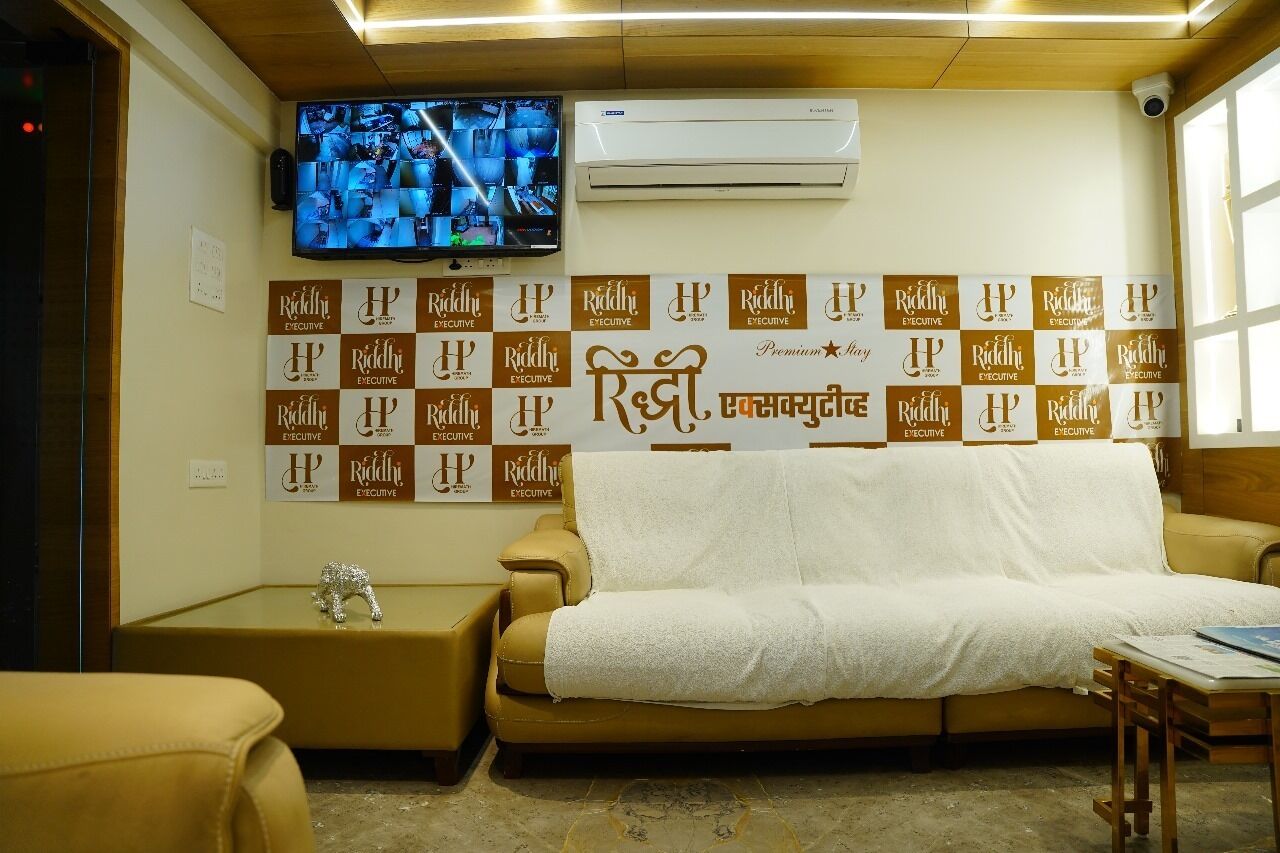 A hotel room with a large wall-mounted television, a sofa, and a small table.