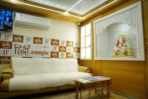 Quarto de hotel com sofá bege, uma pequena mesa de madeira e parede decorada com placas 'Riddhi Executive'.