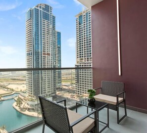 A balcony with a glass railing, two chairs, a small table, and a potted plant.