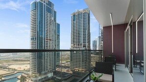 Een balkon met uitzicht op twee wolkenkrabbers, een glazen hekwerk en een kleintje tafeltje met een plant.