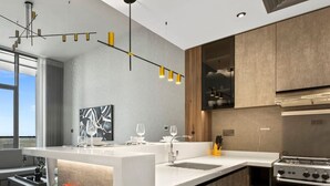 Een moderne keuken met een centraal kookeiland, roestvrijstalen apparatuur en hanglampen.