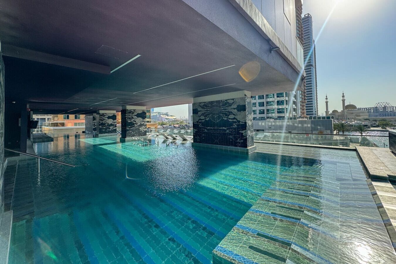 Ein Dachpool im Infinity-Stil mit klarem, blauem Wasser, umgeben von moderner Architektur und Blick auf eine Moschee.