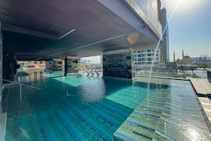 Et rooftop-infinity pool med krystalklart blåt vand, omgivet af moderne arkitektur og udsigt til en moské.