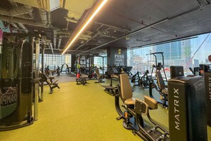 A gym with various exercise equipment, a motivational quote on the wall, and a view of the city through large windows.