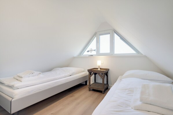 A small, well-lit bedroom with two single beds, a wooden nightstand with a lamp, and a window providing natural light. - "Vacation in vacation home Levi: relaxation and adventure on Sylt!" (Sylt / OT Tinnum)