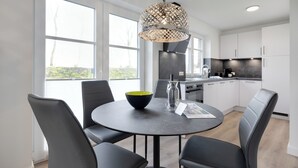 A modern kitchen with white cabinets, a round dining table with black chairs, and a large window providing natural light. - "Vacation in vacation home Levi: relaxation and adventure on Sylt!" (Sylt / OT Tinnum)