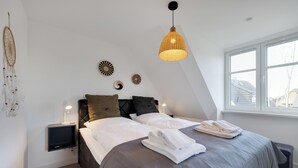 A bedroom with a bed, bedside tables, a hanging light fixture, and wall decor. - "Vacation in vacation home Levi: relaxation and adventure on Sylt!" (Sylt / OT Tinnum)