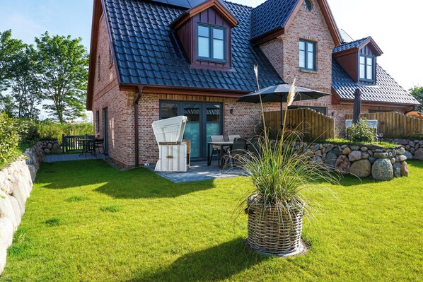 A brick house with a dark tiled roof, a patio with outdoor furniture, and a stone wall.