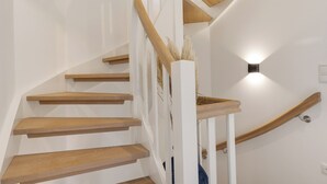 A spiral staircase with wooden steps and white railings, leading to a landing with a wall-mounted light fixture. - "Your perfect vacation paradise on Sylt - the vacation home Lena awaits you!" (Sylt / OT Tinnum)