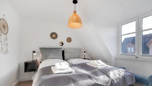A modern bedroom with a large bed, a hanging light fixture, and a view of the outside through a window. - "Your perfect vacation paradise on Sylt - the vacation home Lena awaits you!" (Sylt / OT Tinnum)