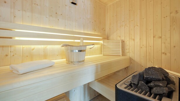 A sauna with wooden walls, a bench, a bucket, and a pile of stones. - "Your perfect vacation paradise on Sylt - the vacation home Lena awaits you!" (Sylt / OT Tinnum)