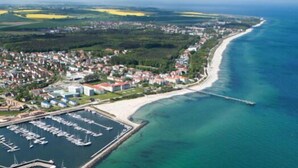Vista aérea de un pueblo costero con un puerto deportivo, una playa y zonas residenciales.