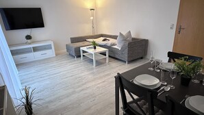 Una sala de estar moderna con un sofá gris, una mesa de centro blanca y un televisor de pantalla plana montado en la pared.