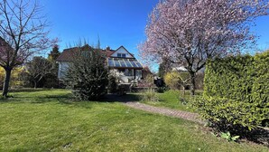Una casa con techo inclinado, un invernadero de vidrio y un jardín bien cuidado con árboles en flor.