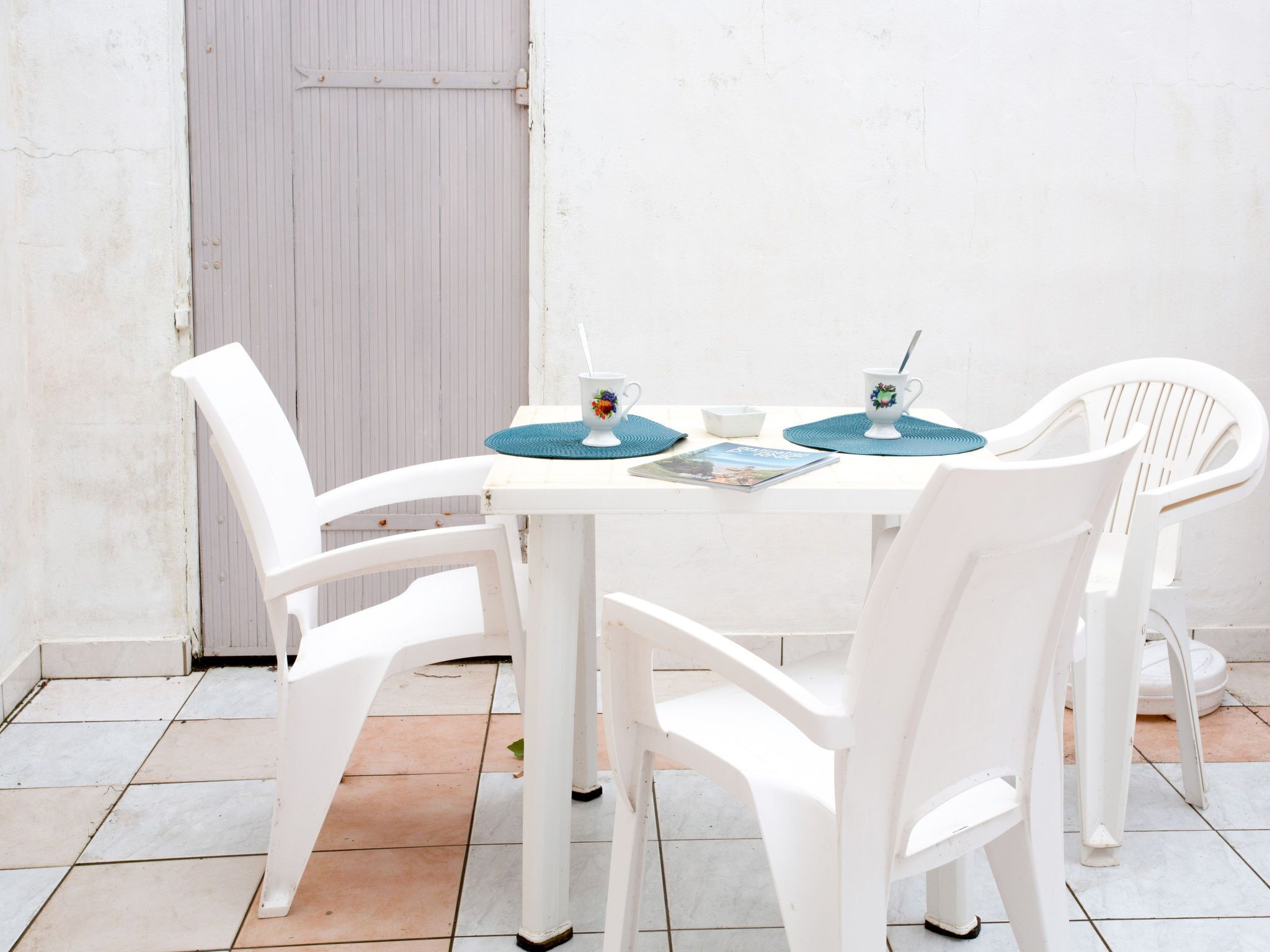 Uma mesa branca com quatro cadeiras, uma porta fechada e um chão de azulejos.