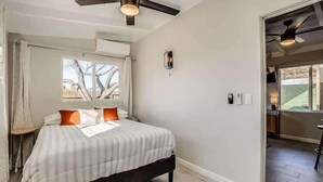 Un dormitorio con cama, ventilador de techo, ventana con cortinas y vistas al exterior.