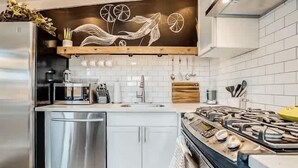 Una cocina moderna con un refrigerador de acero inoxidable, lavavajillas, estufa a gas y encimera de madera.