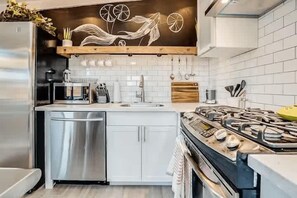A modern kitchen with a stainless steel refrigerator, a dishwasher, a gas stove, and a wooden countertop.