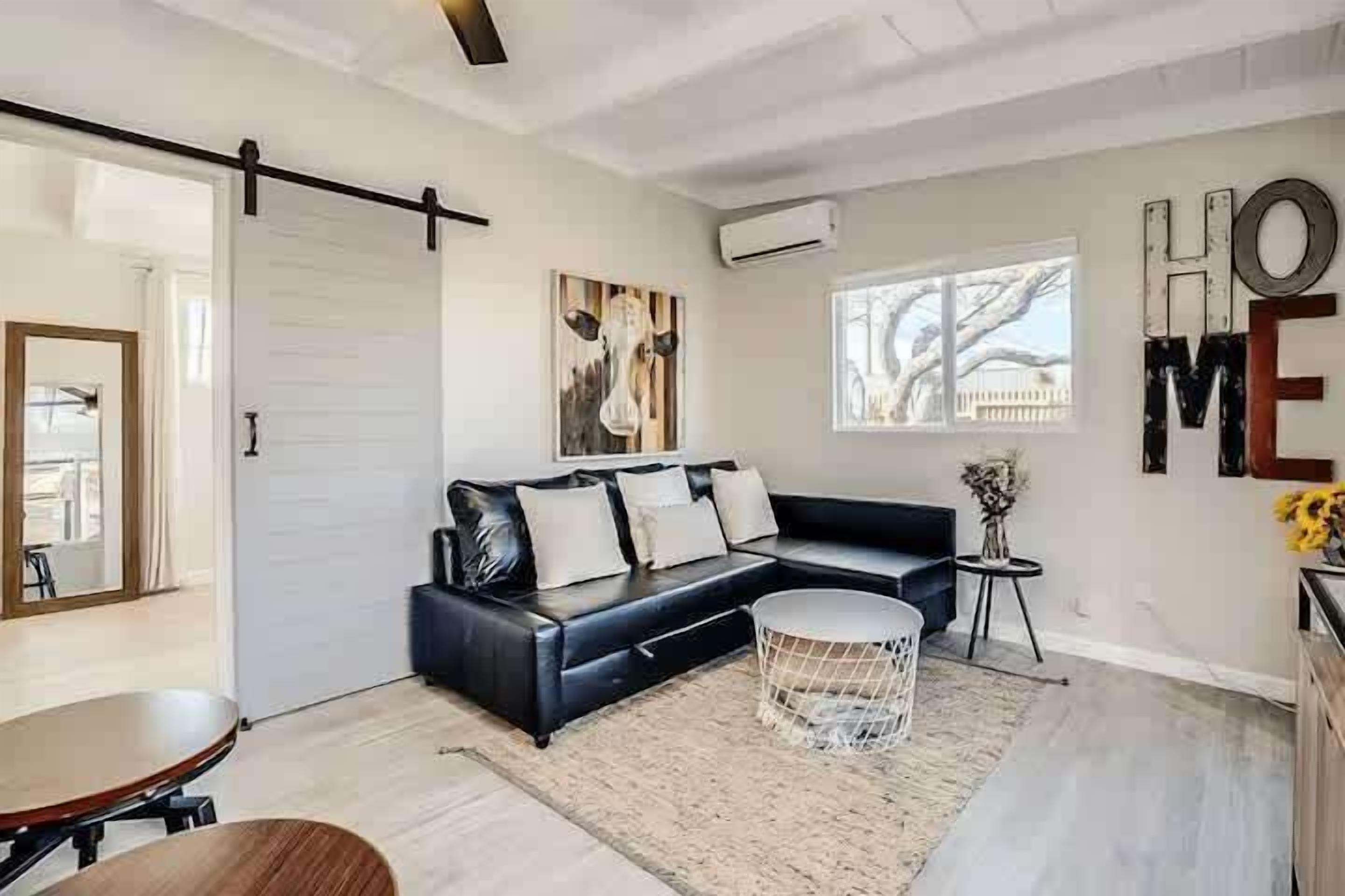 Una sala de estar moderna con un sofá de cuero negro, una mesa de centro redonda y un ventanal amplio.