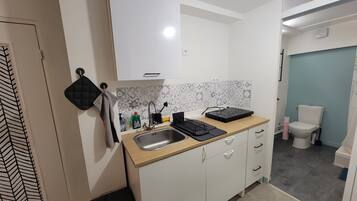 Een kleine keuken met een spoelbak, aanrecht en een toilet in de aangrenzende ruimte.