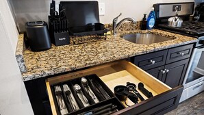 Una cocina con encimeras de granito, un fregadero, una estufa y un organizador de cajones con utensilios.