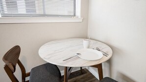 Un comedor con una mesa redonda de mármol, dos sillas, un plato blanco, una taza y cubiertos.
