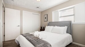 Un dormitorio ordenado con una cama grande, una mesita de noche y un ventanal con persianas.