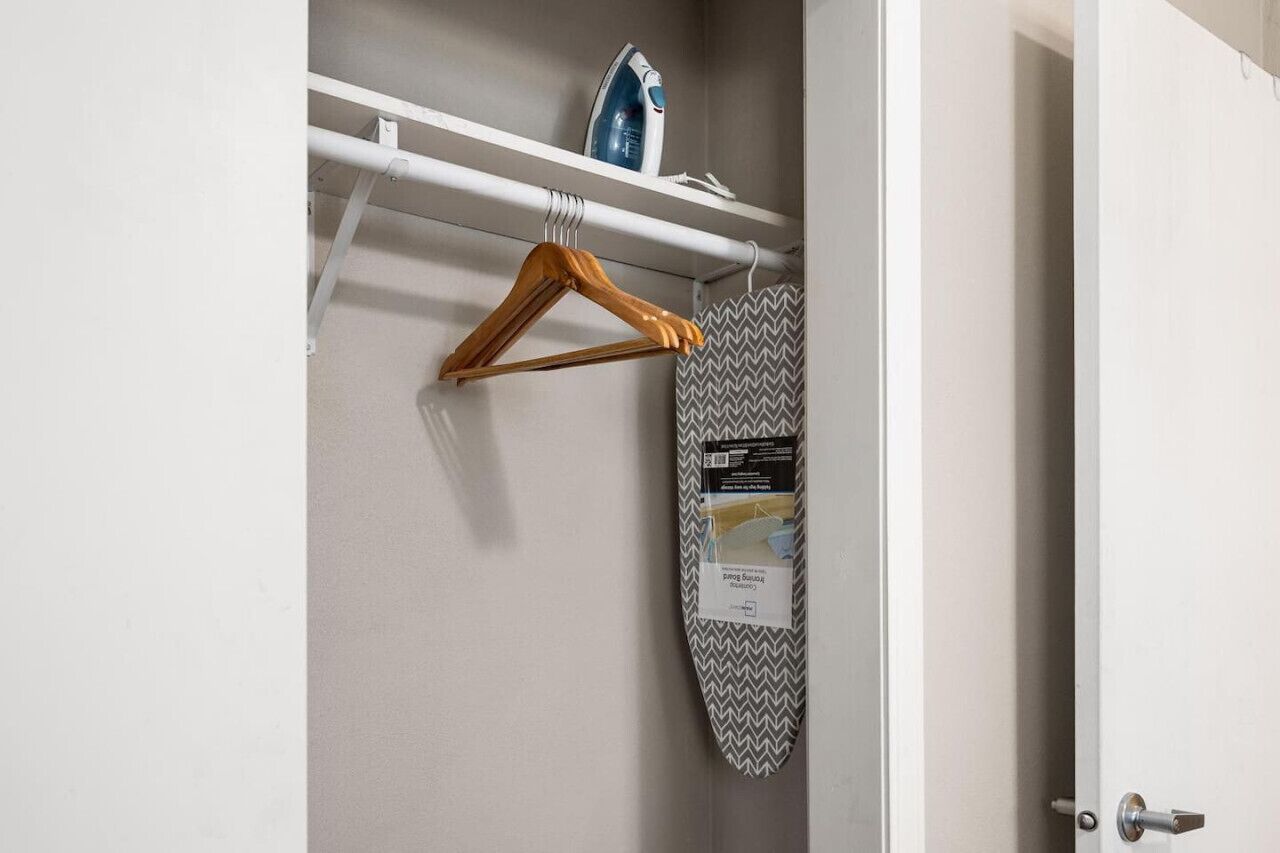 A white door with a wooden hanger and a patterned ironing board leaning against it.