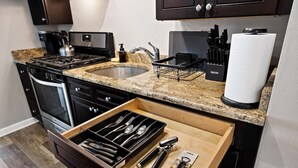 A kitchen with dark cabinetry, a granite countertop, a stainless steel sink, and a drawer organizer with utensils. - A Trendy Escape close to Downtown Peoria (Peoria)