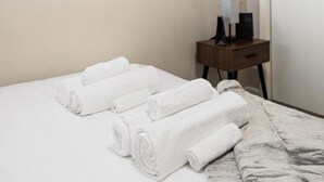 A neatly made bed with rolled white towels, a wooden nightstand with a lamp, and a door in the background. - A Trendy Escape close to Downtown Peoria (Peoria)