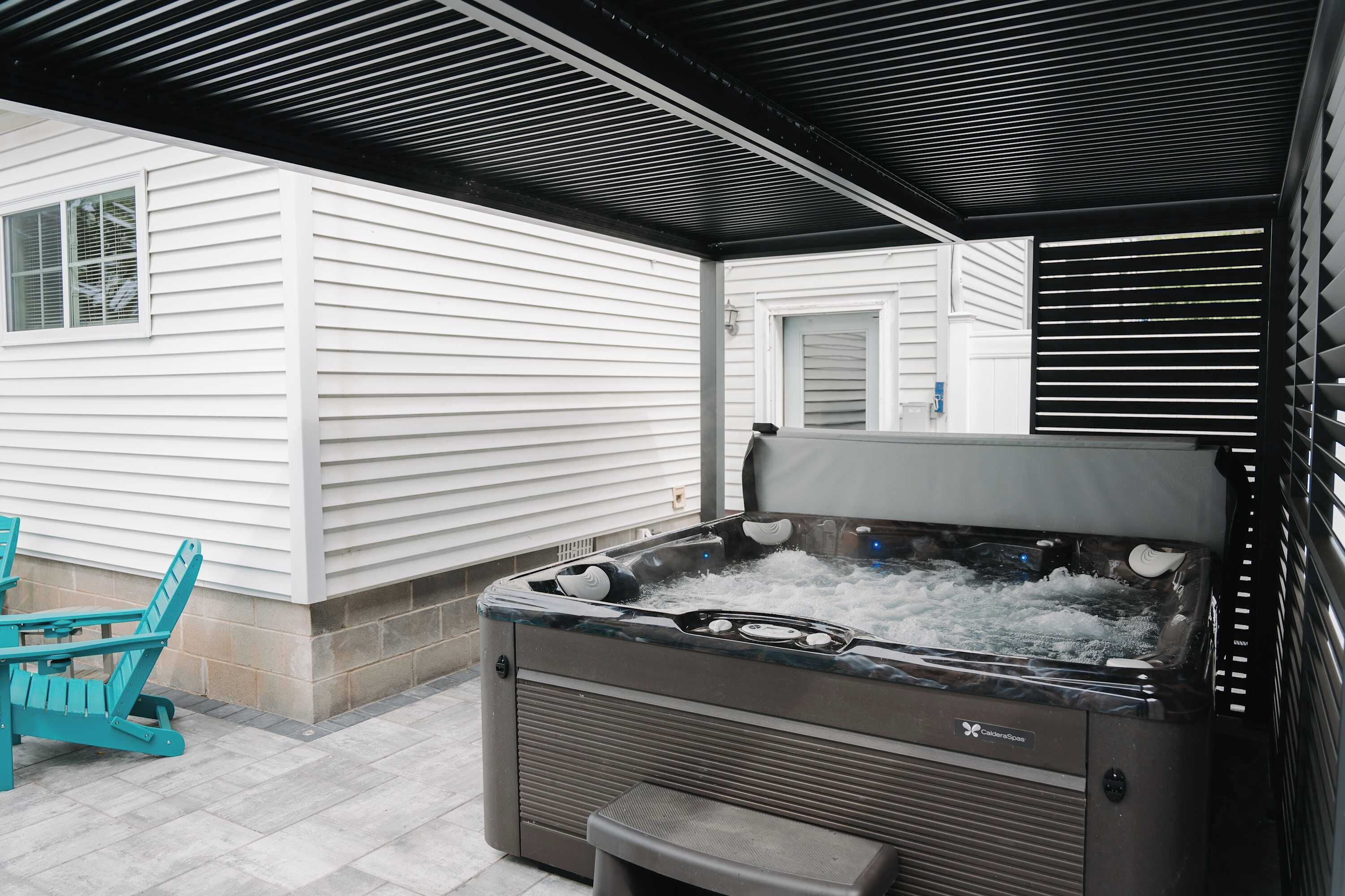 A hot tub with a control panel, a chair, and a covered patio area.