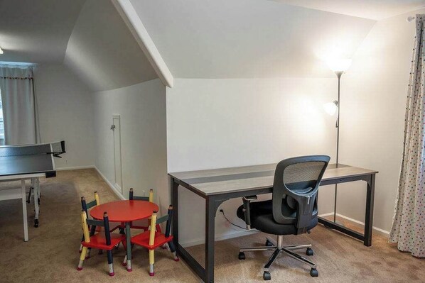 A room with a desk, office chair, and a ping pong table.