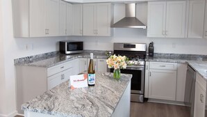 Una cucina moderna con mobili bianchi, un piano di lavoro in granito, una cappa aspirante in acciaio inossidabile, un forno a microonde e una bottiglia di vino.
