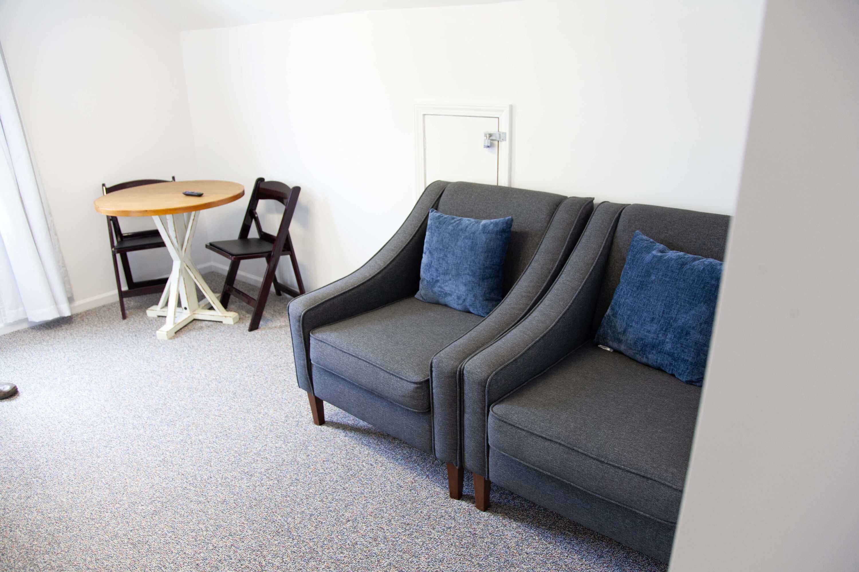 Un salon avec un canapé gris, deux coussins bleus, une table basse en bois et deux chaises en bois.