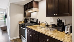 Eine moderne Küche mit dunklen Holzausziehtüren, einer Granitarbeitsplatte, Edelstahlgeräten und einem eingebauten Backofen.