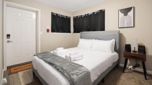 Ein Hotelzimmer mit einem Bett, einem Nachttisch mit zwei Lampen, einer Tür und einem Fenster mit Vorhängen.