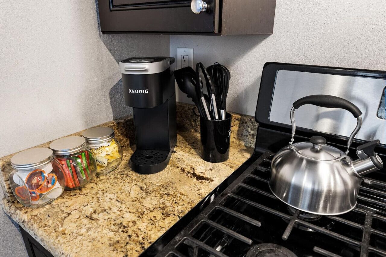 Een keuken met een Keurig koffiezetapparaat, een waterkoker en kruidenpotjes op het aanrecht.