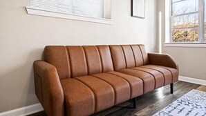 Ein braunes Ledersofa vor einer Wand mit Fenster und Jalousien.