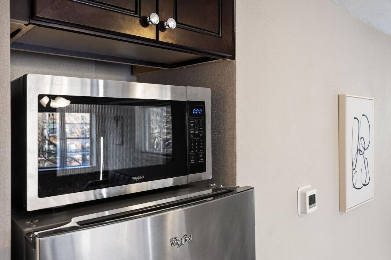 Un horno microondas Whirlpool de acero inoxidable montado sobre un refrigerador, con pantalla digital y panel de control.