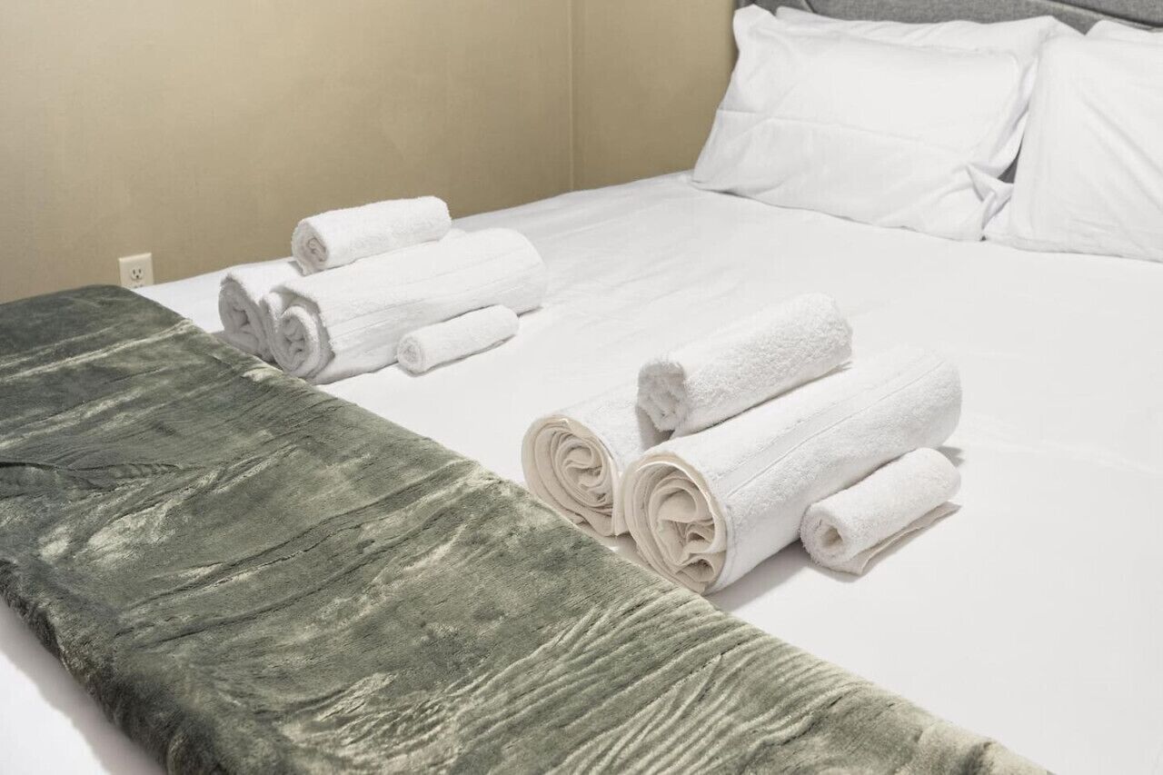 Una cama bien hecha con sábanas blancas y toallas enrolladas.