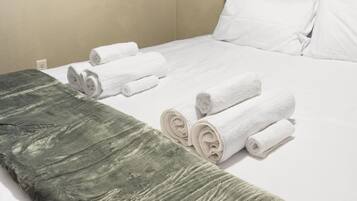 Una cama bien hecha con sábanas blancas y toallas enrolladas.