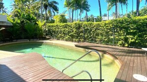 A swimming pool with a wooden deck, surrounded by lush greenery and palm trees.