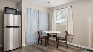 Cozinha compacta com geladeira, micro-ondas, mesa de jantar para duas pessoas e janela com persianas.