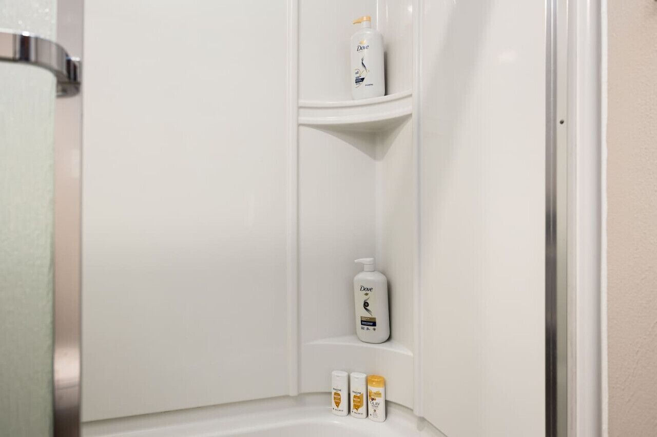 A bathroom with a white sink, a mirror, and toiletries on a shelf.