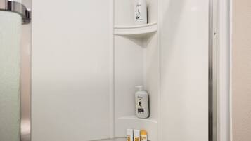 A bathroom with a white sink, a mirror, and toiletries on a shelf.