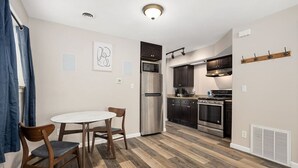 Una cocina moderna con armarios oscuros, electrodomésticos de acero inoxidable y una mesa de comedor blanca con sillas.