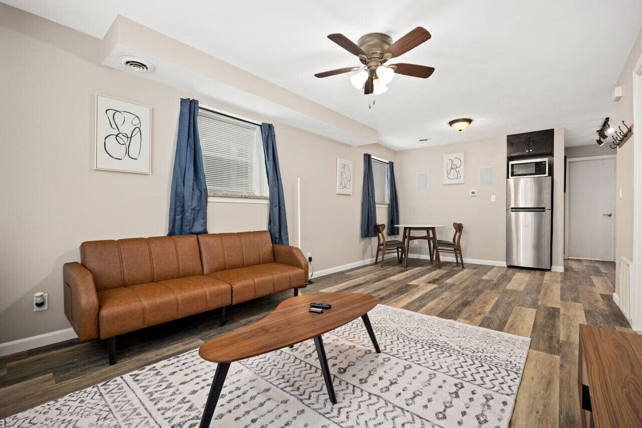 A modern living room with a brown leather sofa, a wooden coffee table, and a ceiling fan.
