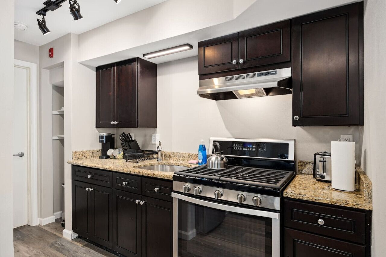 A modern kitchen with dark wood cabinets, a stainless steel range, a built-in oven, and granite countertops.